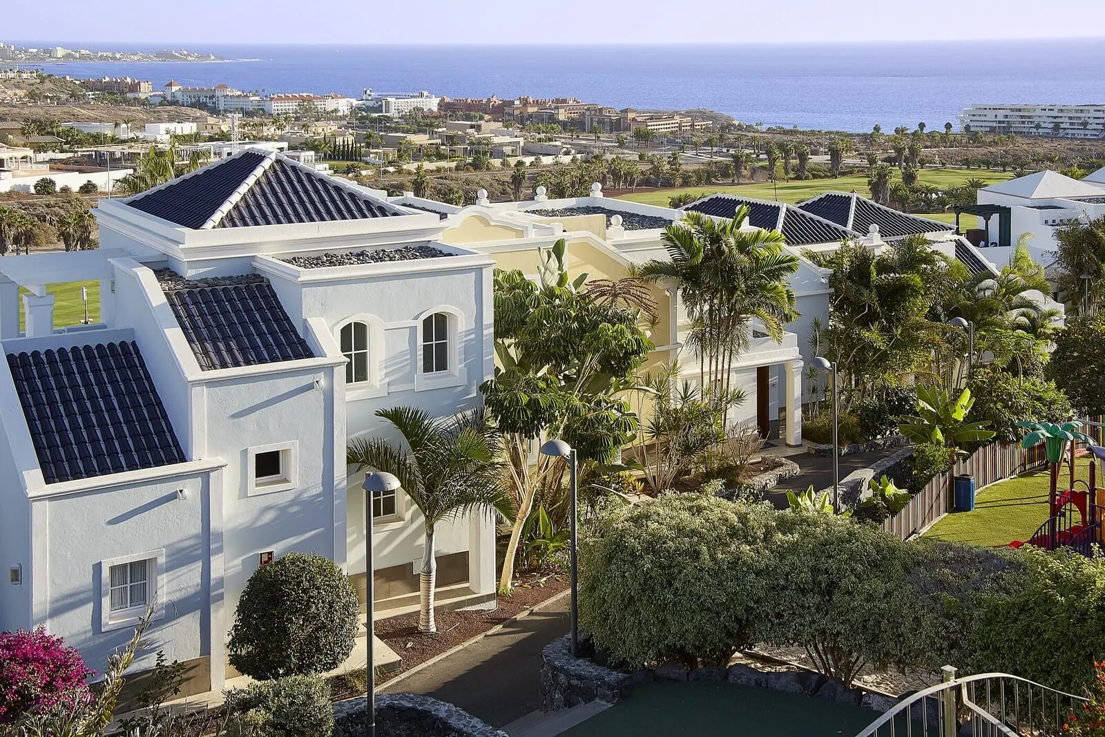 Hotel Suite Villa María: A residential area with white buildings, solar panels, and a view of the ocean