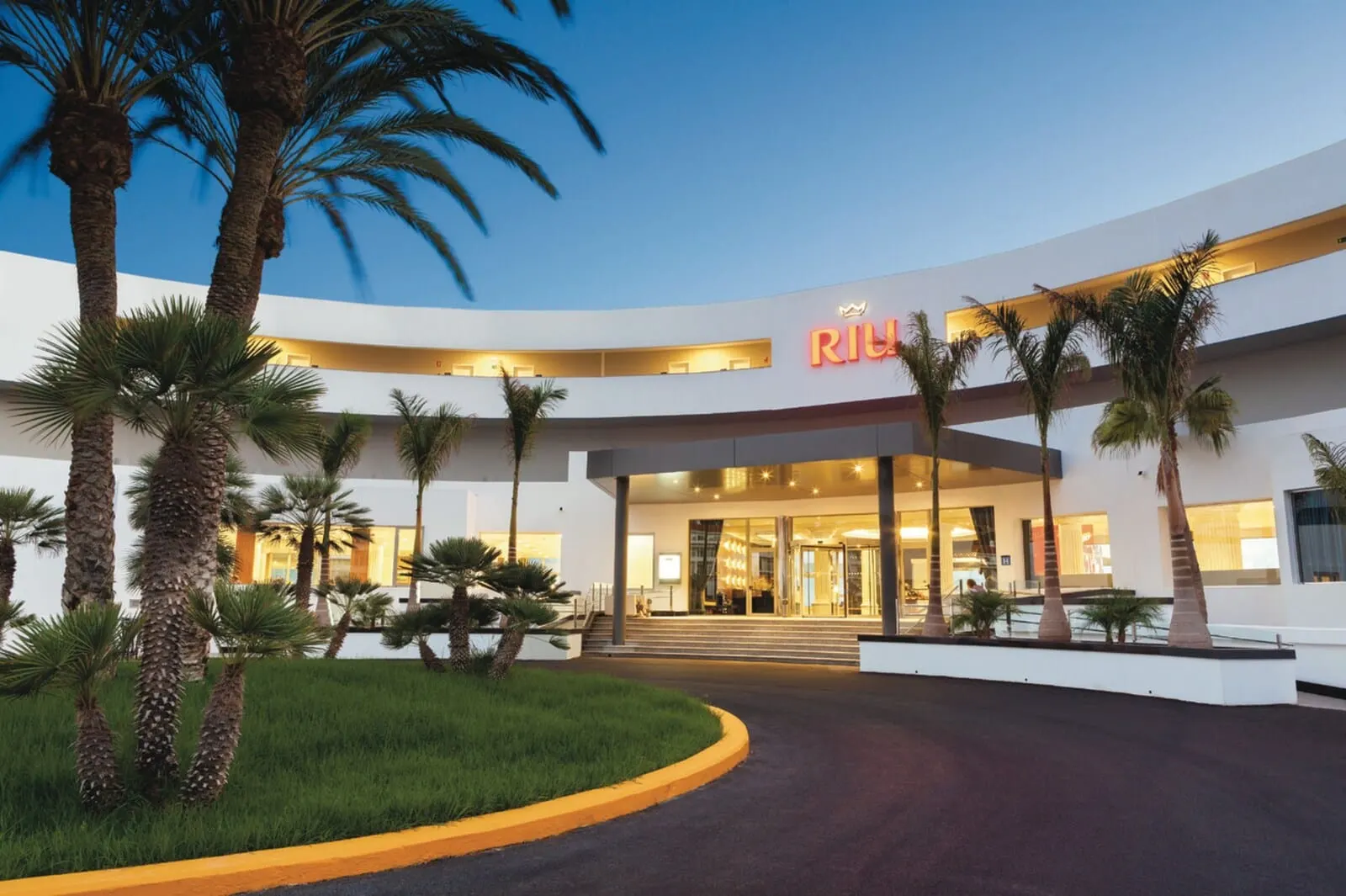 Hotel Riu Palace Tenerife: A modern hotel with a curved facade, palm trees, and a well-lit entrance