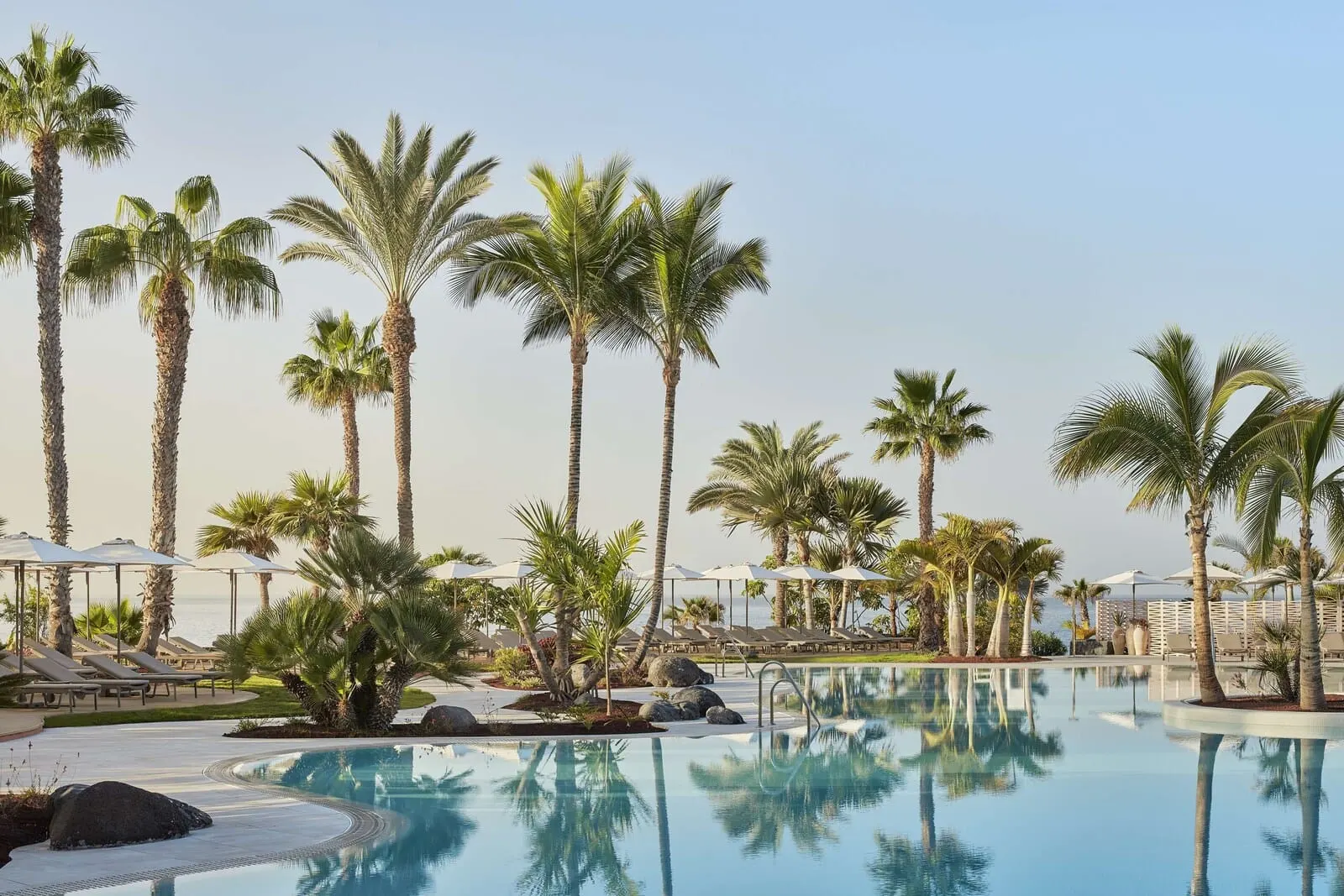 Tivoli La Caleta Tenerife Resort: A pool area with palm trees, lounge chairs, and umbrellas
