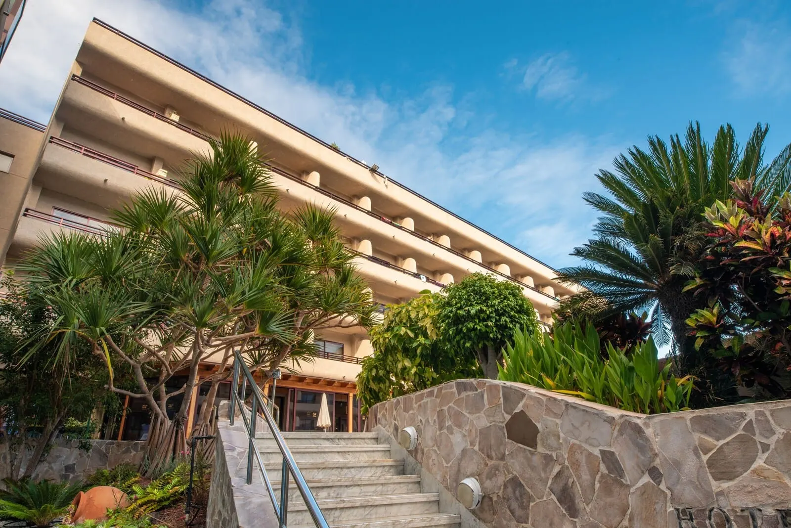 GF Fañabé: A hotel with a stone staircase, palm trees, and a clear blue sky