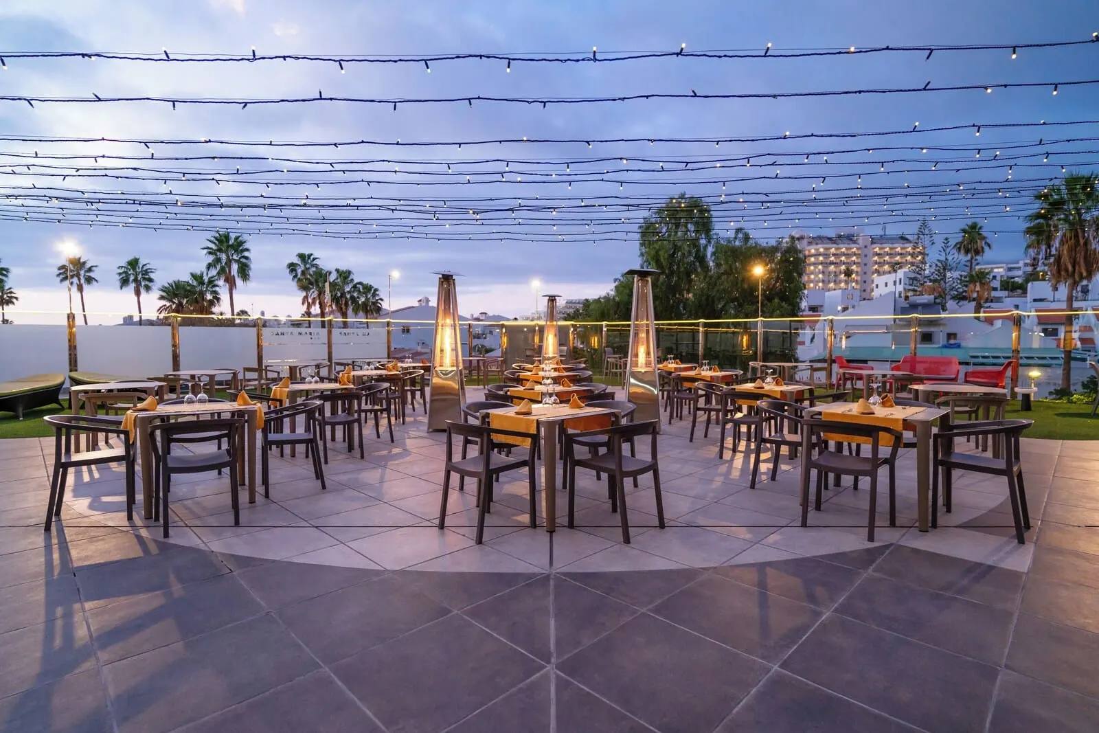 HOVIMA Santa María: An outdoor dining area with multiple tables and chairs, string lights overhead