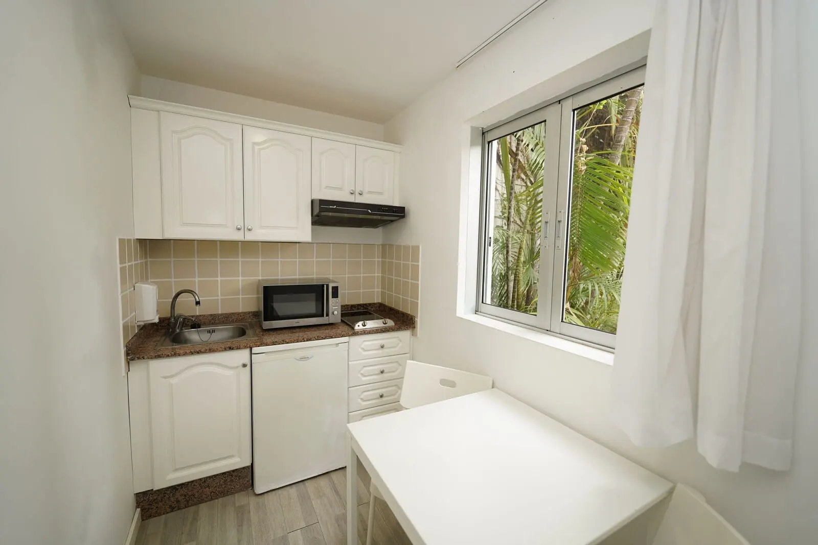 Hotel RF San Borondón: A compact kitchen with white cabinets, a microwave, and a window with curtains
