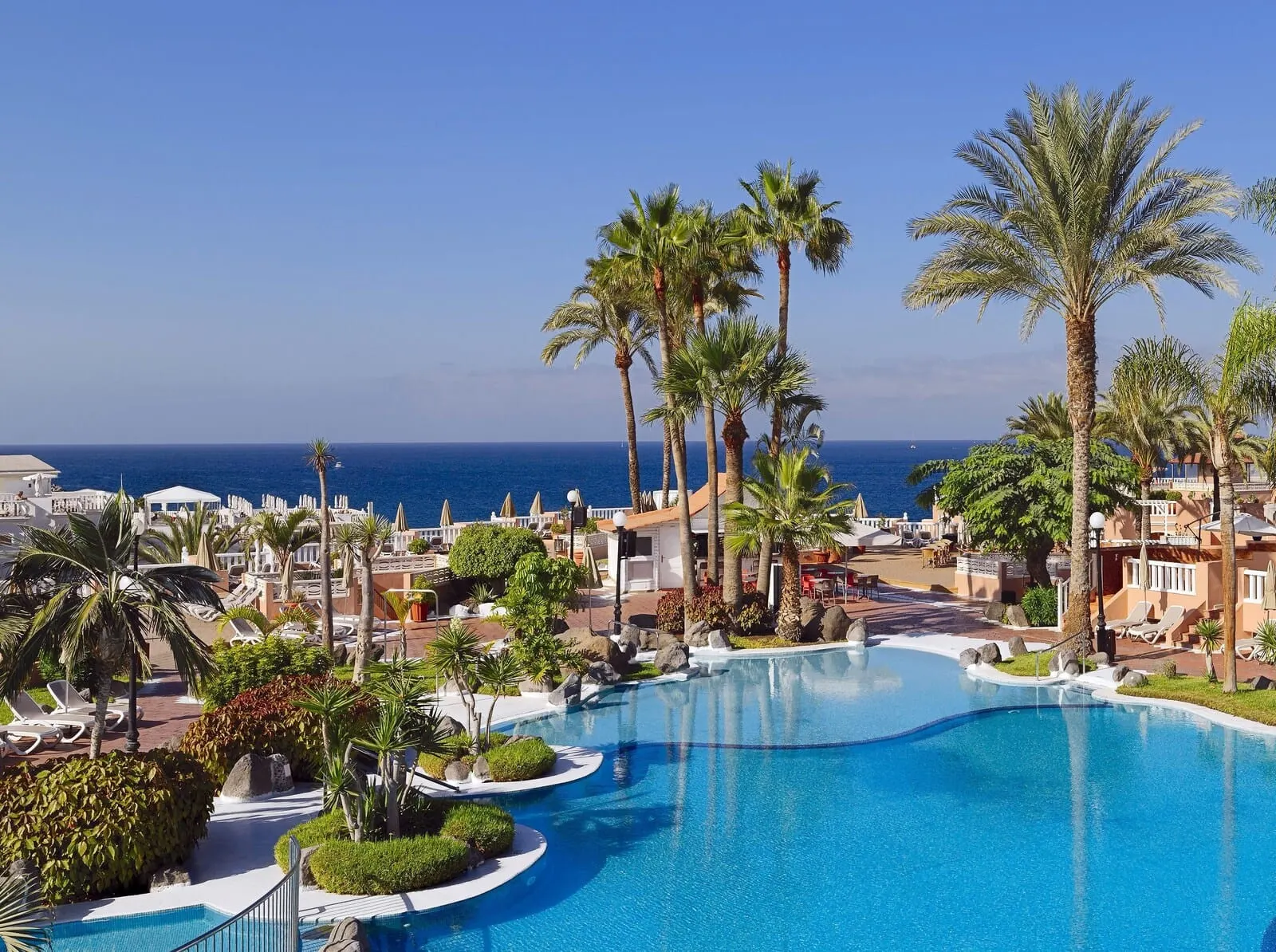 Sol Sun Beach Apartamentos: A resort pool area with palm trees, lounge chairs, and a view of the ocean