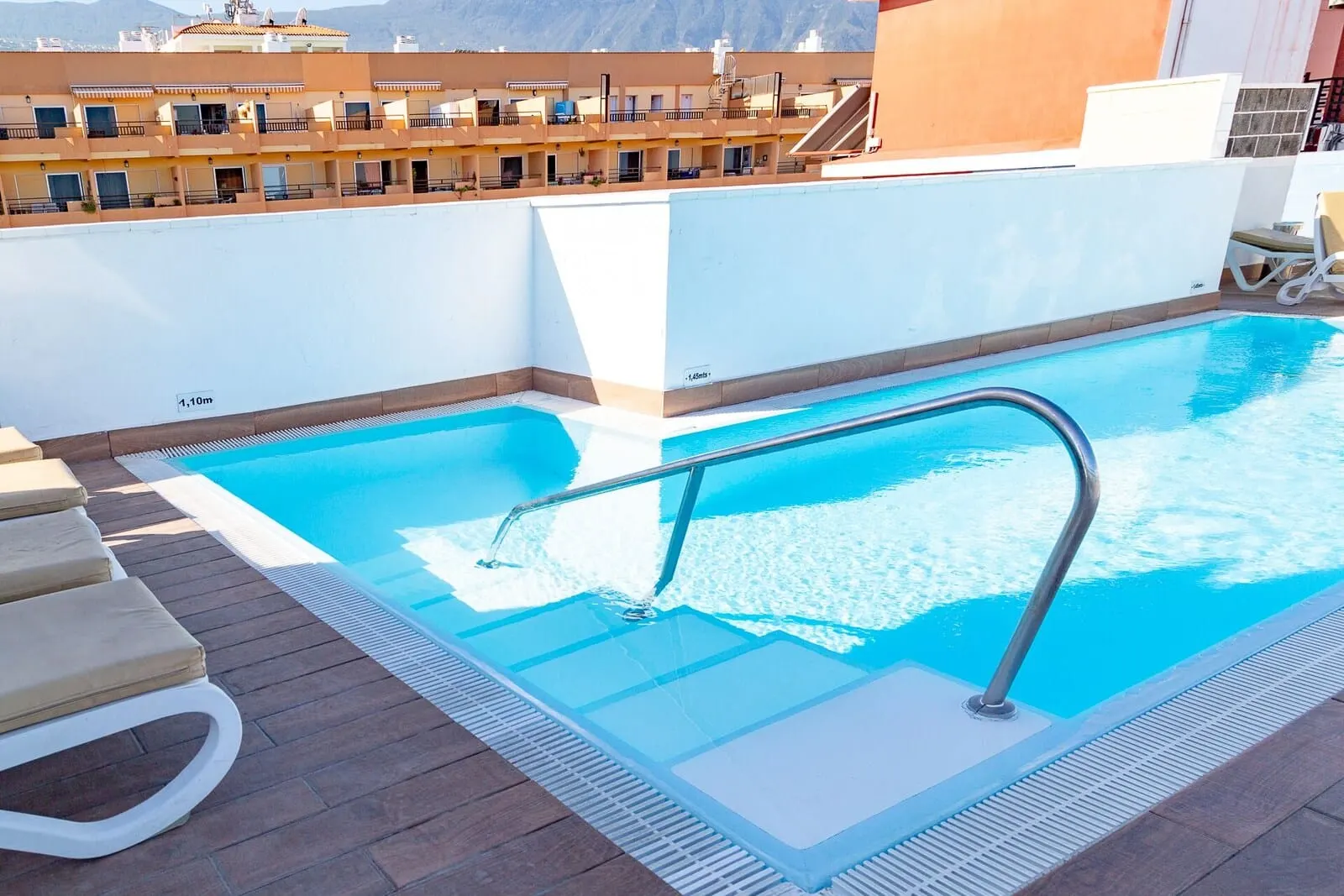 Hotel Tropical: A rooftop pool with a metal ladder, lounge chairs, and a view of a mountain range