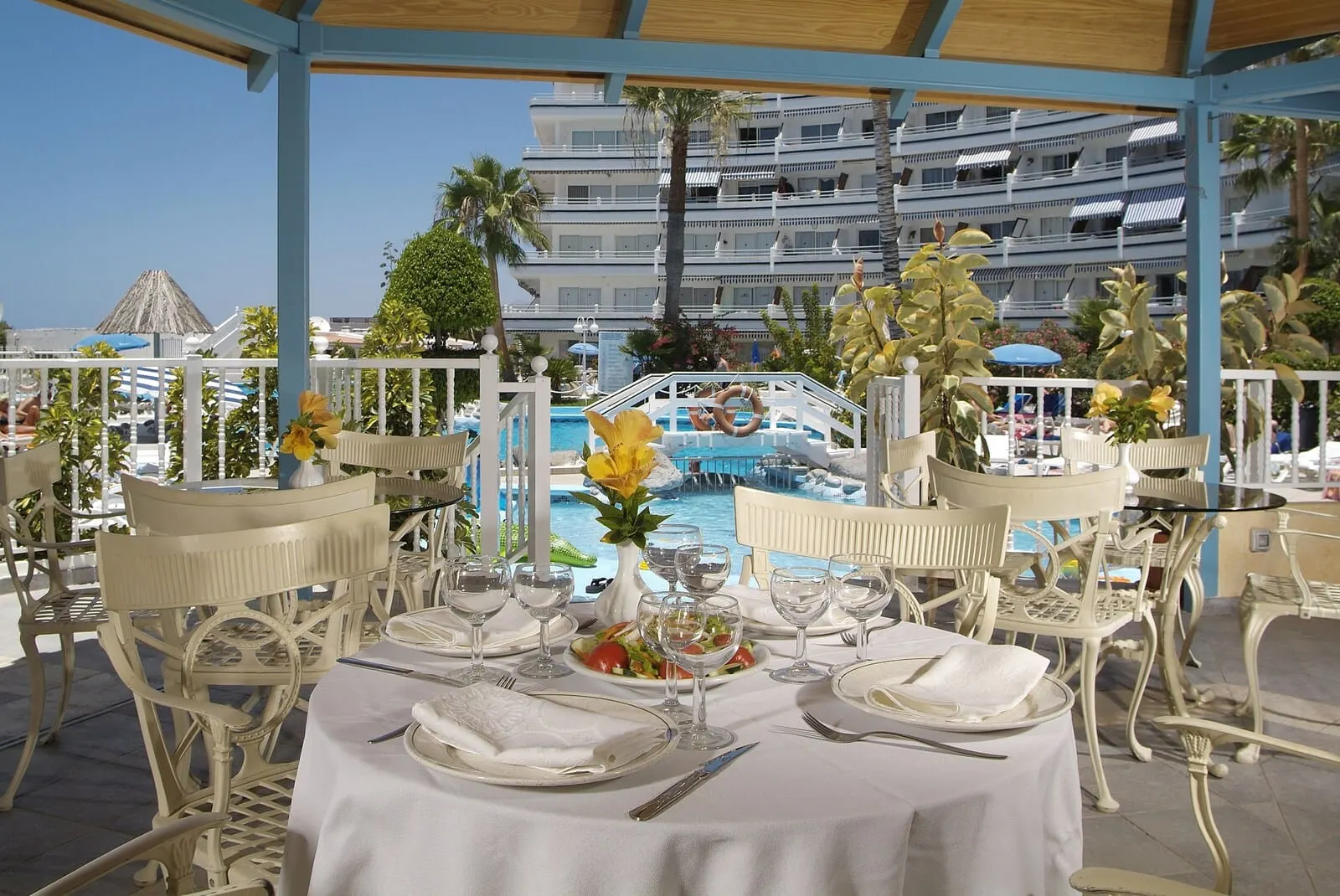 HOVIMA Atlantis: An outdoor dining area with white tables and chairs, a pool in the background