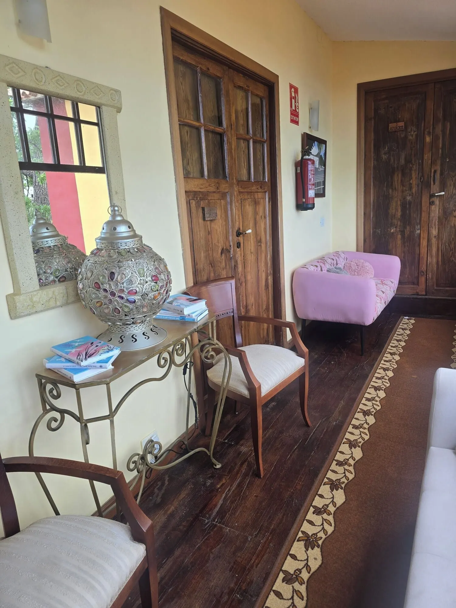 Hotel Rural La Raya 1866: A room with a wooden door, a table with books, a chair, and a pink ottoman